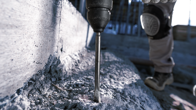 Một người mặc đồ bảo hộ đang khoan vào bê tông bằng búa quay.