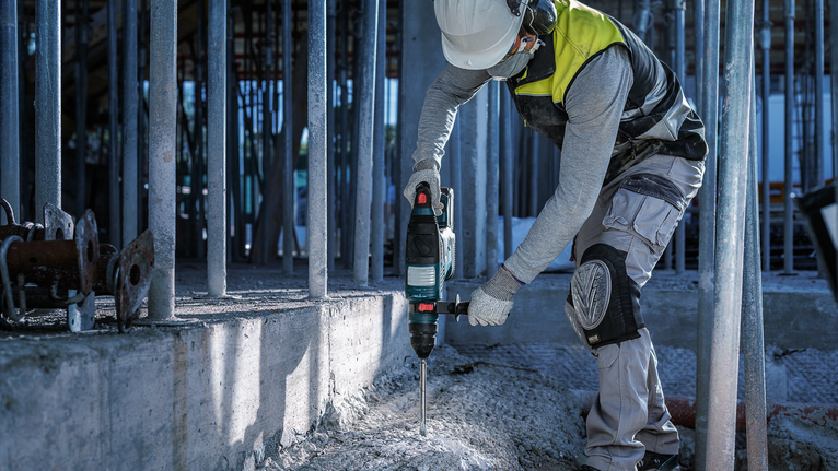 Một người mặc đồ bảo hộ đang khoan bê tông tại một công trường xây dựng.