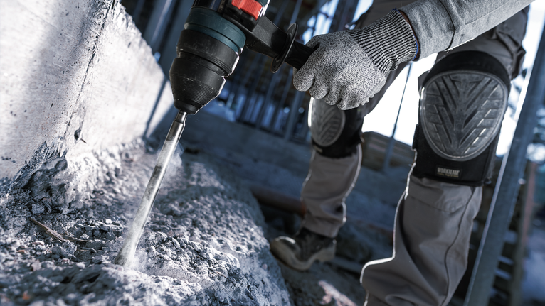 Một người mặc đồ bảo hộ sử dụng búa quay để khoan vào bê tông.