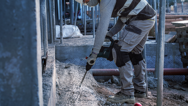 Người mặc đồ bảo hộ đang phá bê tông bằng dụng cụ điện tại công trường xây dựng.