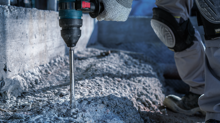 Một người mặc đồ bảo hộ đang khoan bê tông tại một công trường xây dựng.