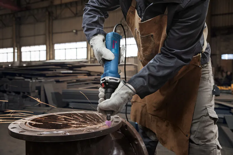 Một người mặc đồ bảo hộ sẽ mài kim loại bằng máy mài thẳng, tạo ra tia lửa điện.