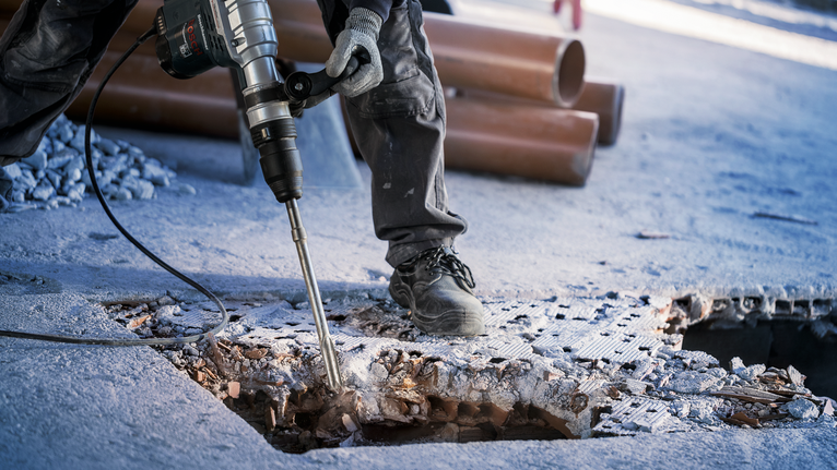 Một người mặc đồ bảo hộ đang phá bê tông bằng búa quay.