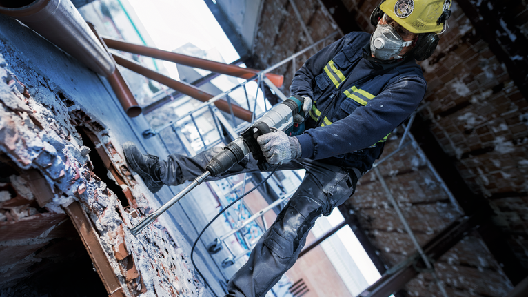 Một người mặc đồ bảo hộ sử dụng búa quay để phá vỡ đống đổ nát bê tông.