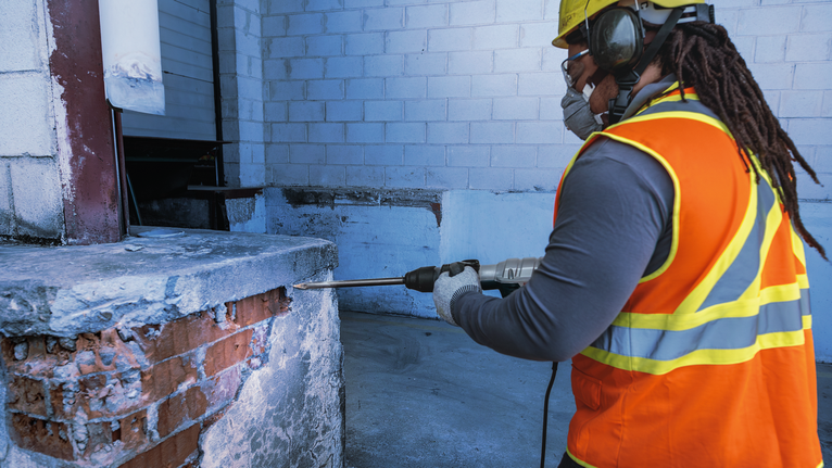 Người đeo thiết bị an toàn đang khoan vào tường bê tông tại một công trường xây dựng.