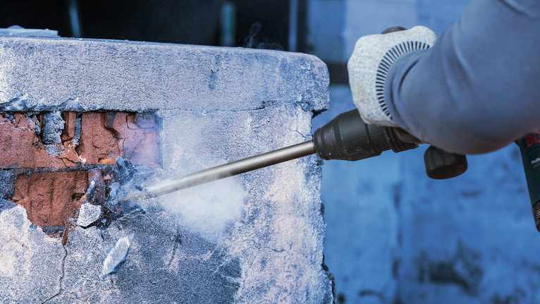 Người mặc thiết bị an toàn sử dụng công cụ phá dỡ để phá vỡ bức tường bê tông.