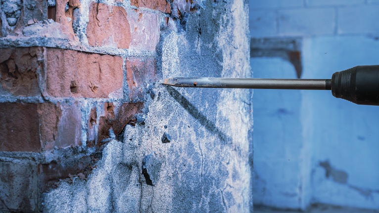 Máy khoan đục phá vỡ bê tông khỏi bức tường gạch.