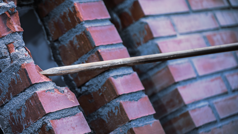 Chiếc đục nhọn đục thủng bức tường gạch đỏ.