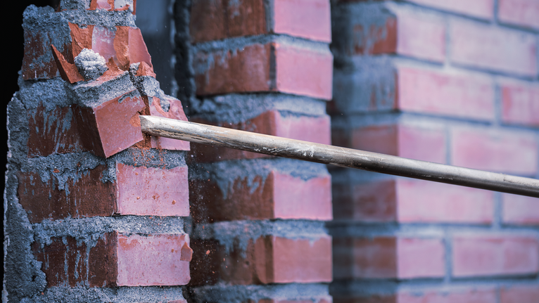 Thanh phá dỡ đang phá vỡ những viên gạch đỏ ra khỏi bức tường vữa.