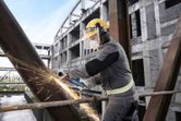 Một người mặc đồ bảo hộ đang mài một thanh kim loại tại công trường xây dựng.