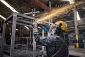 Một người mặc đồ bảo hộ sẽ mài một khung kim loại, tạo ra những tia lửa sáng.