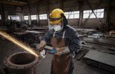 Một người mặc đồ bảo hộ đang mài kim loại bằng dụng cụ điện trong nhà máy.