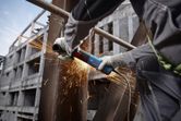 Một người mặc đồ bảo hộ mài một thanh thép, tạo ra tia lửa sáng.