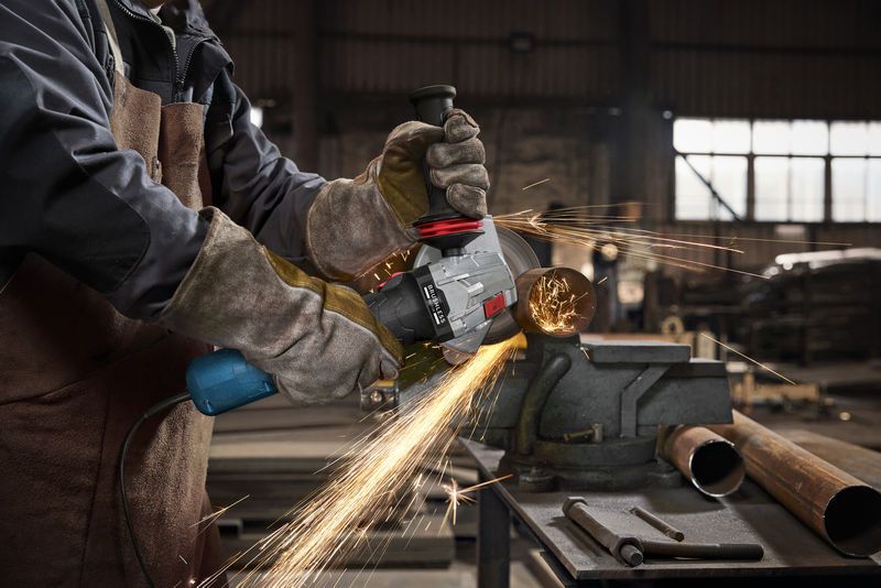 Một người mặc đồ bảo hộ mài một ống kim loại, tạo ra tia lửa sáng.