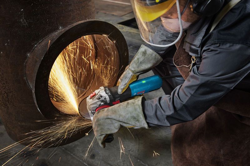 Một người mặc đồ bảo hộ mài một ống kim loại lớn, tạo ra tia lửa sáng.