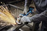 Một người mặc đồ bảo hộ đang mài khung kim loại bằng máy mài góc.
