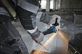 Một người mặc đồ bảo hộ đang cắt kim loại bằng máy mài góc có tia lửa bắn ra.