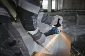 Một người mặc đồ bảo hộ đang cắt kim loại bằng máy mài góc có tia lửa bắn ra.