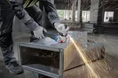 Một người mặc đồ bảo hộ mài ống dẫn kim loại, tạo ra tia lửa.