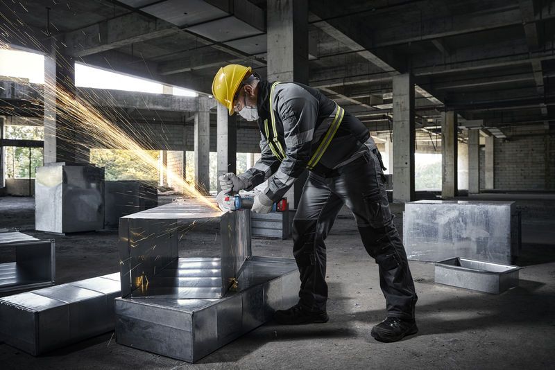 Một người mặc đồ bảo hộ đang sử dụng máy mài góc trên ống dẫn kim loại tại công trường xây dựng.