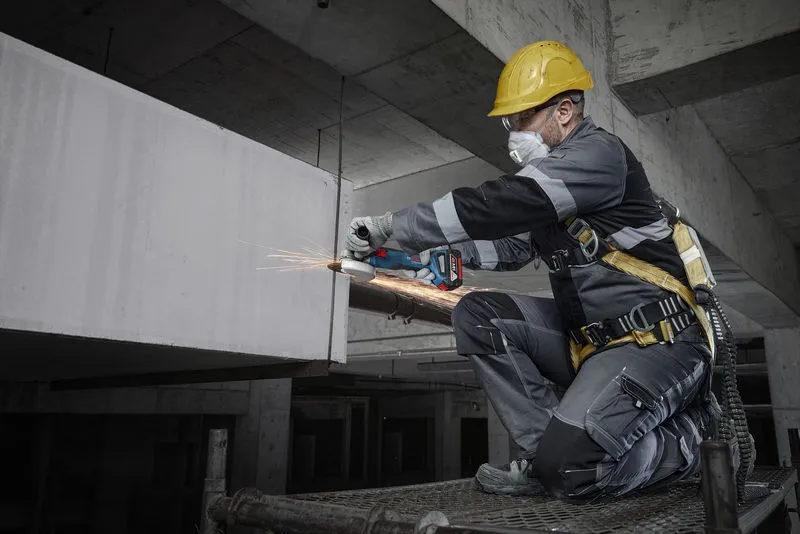 Một người mặc đồ bảo hộ đang mài bê tông bằng dụng cụ điện tại công trường xây dựng.