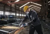 Một người mặc đồ bảo hộ đang mài kim loại, tạo ra tia lửa sáng trong nhà máy.