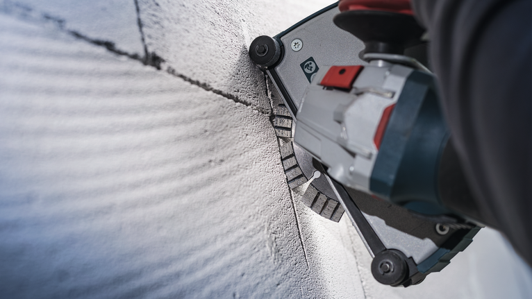 Người đeo thiết bị an toàn sử dụng dụng cụ điện để cắt một rãnh thẳng trên bê tông.