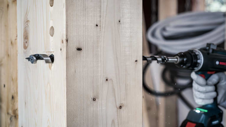 Bộ mũi khoan xoắn ốc PRO Wood, L235, 6 chiếc Người mặc thiết bị an toàn sử dụng máy khoan điện để khoan vào một thanh gỗ.