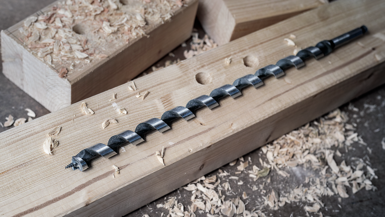 Mũi khoan xoắn đặt trên một thanh gỗ được bao quanh bởi các mảnh gỗ vụn.