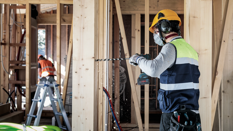 Bộ mũi khoan xoắn ốc PRO Wood, L235, 6 chiếc Người đeo thiết bị an toàn đang khoan vào dầm gỗ tại công trường xây dựng.