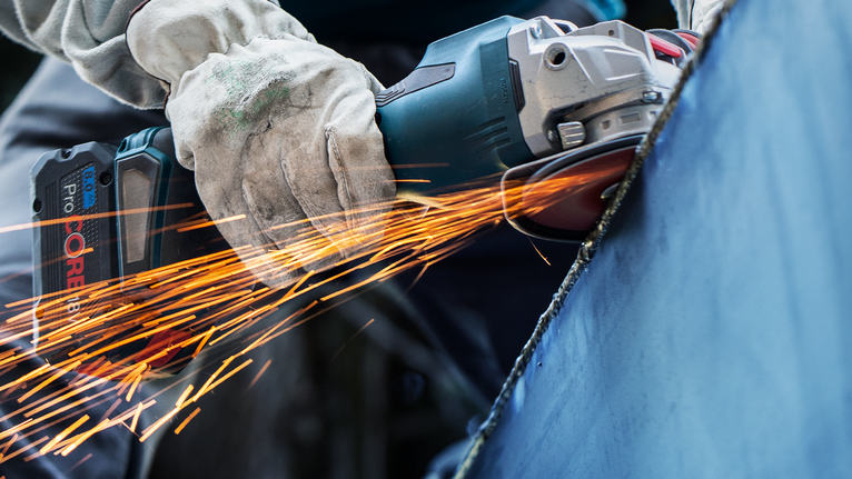 Một người đeo thiết bị an toàn mài kim loại bằng dụng cụ điện, tạo ra tia lửa.