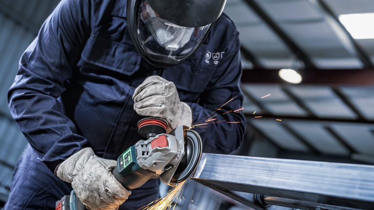 Một người mặc đồ bảo hộ sẽ mài kim loại, tạo ra tia lửa.