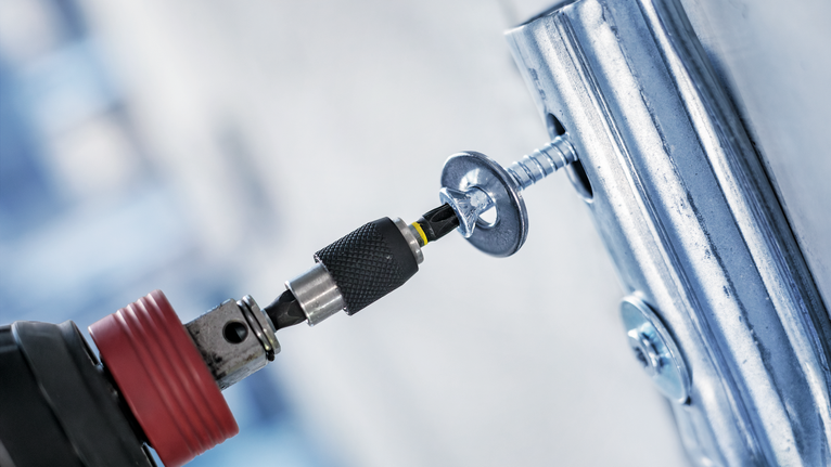 Máy khoan không dây đang bắt vít vào khung kim loại.