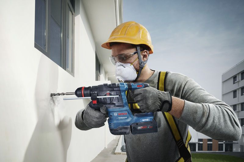 GBH 18V-22 X Một người mặc đồ bảo hộ đang khoan vào bức tường bên ngoài bằng một dụng cụ điện.