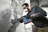Một người mặc đồ bảo hộ sử dụng búa quay để tháo gạch ra khỏi tường.