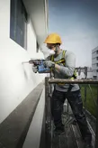 Công nhân mặc đồ bảo hộ đang khoan vào mặt tiền tòa nhà trong khi đứng trên giàn giáo.