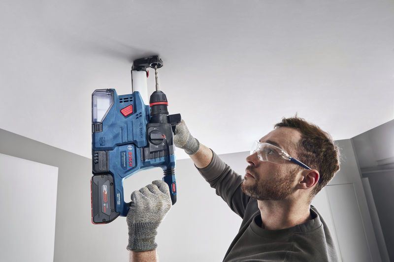 GBH 18V-22 X Một người mặc đồ bảo hộ đang khoan trần nhà bằng búa quay không dây.