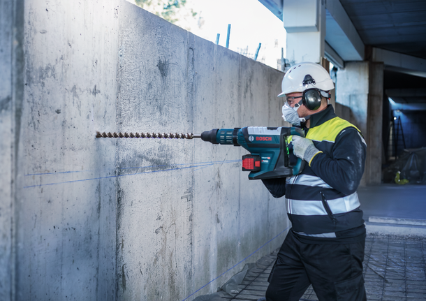 Người đeo thiết bị an toàn khoan vào tường bê tông bằng búa quay lớn.