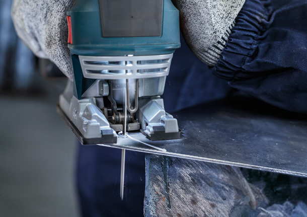 Người mặc đồ bảo hộ đang cắt tấm kim loại bằng máy cưa lọng.