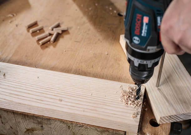 Bộ mũi khoan đầu đinh nhỏ PRO Wood, 7 chiếc Người đang sử dụng máy khoan điện để khoan lỗ trên tấm ván gỗ trên bàn làm việc.