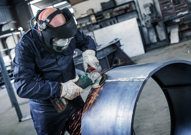 Người đeo thiết bị an toàn mài một ống kim loại lớn, tạo ra tia lửa.