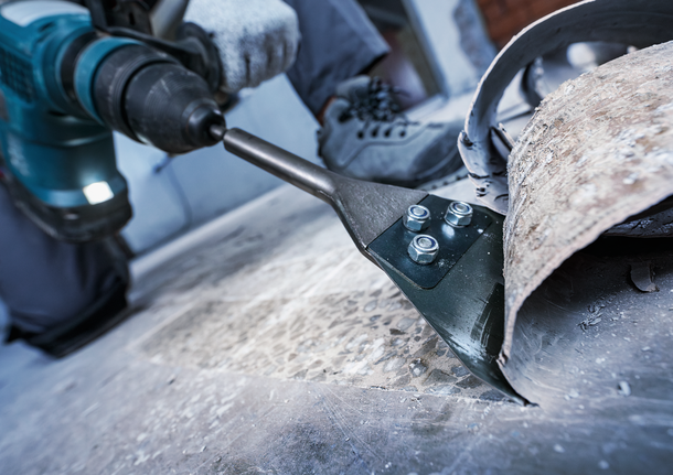 Một người mặc đồ bảo hộ đang sử dụng dụng cụ điện để tháo sàn.