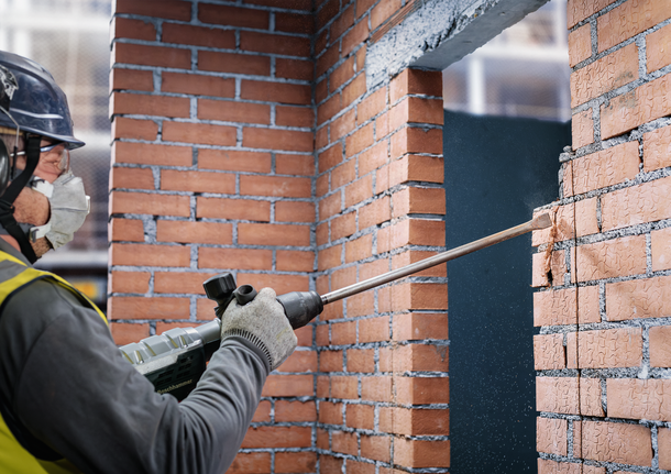 Người mặc đồ bảo hộ sử dụng dụng cụ điện để đục tường gạch.