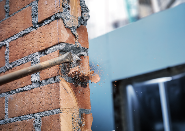 Búa phá dỡ phá vỡ bức tường gạch đỏ tại một công trường xây dựng.