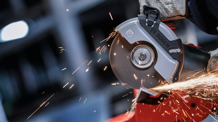 Đá cắt liên kết PRO Metal, 125 x 1,6 x 22,23 mm, X-Lock Một người mặc đồ bảo hộ sẽ mài kim loại, tạo ra tia lửa sáng.