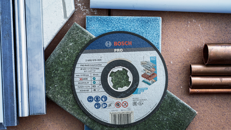 Đá cắt X-Lock PRO Multi Material, 125 x 1 x 22,23 mm Đĩa cắt được đặt trên gạch màu, xung quanh là ống kim loại và ống nhựa.