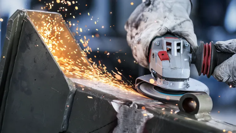 Người đeo thiết bị an toàn đang mài kim loại bằng máy mài góc, tạo ra tia lửa.