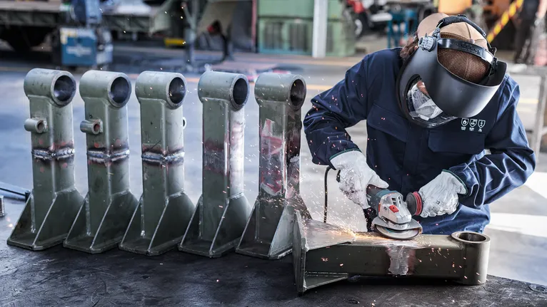 Người mặc đồ bảo hộ mài các bộ phận kim loại, tạo ra tia lửa trong xưởng.