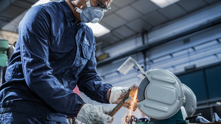 Người mặc đồ bảo hộ sử dụng cưa kim loại để cắt ống, tạo ra tia lửa.