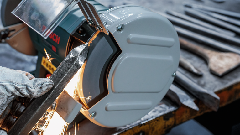 Người đeo thiết bị an toàn mài kim loại trên máy mài có tia lửa bắn ra.